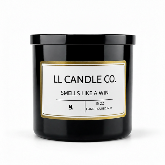 A black glass jar candle with a white label and gold border, reading 'LL CANDLE CO. SMELLS LIKE A WIN' on a clean white background.